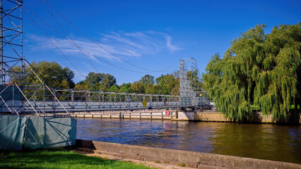 Temporary pedestrian bridge made of metal scaffolding construction across the river on a sunny summer day. Urban engineering solution in the park environment.
