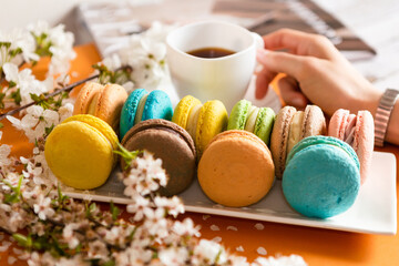 Many classic macaroons on white dishes, on an orange background in natural light