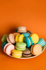 Large round plate full of colorful macaroons on an orange solid background