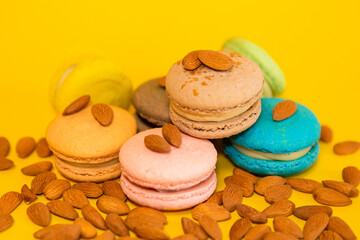 a bunch of macaroons of different colors on a yellow background, with scattered almonds all around