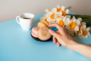 Delicious sweet breakfast with macaroons with coffee, on a blue background with flowers nearby
