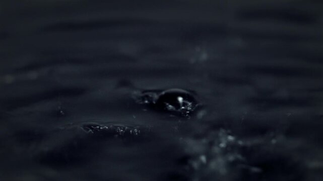 Water drops. Dark abstract macro scene showing droplets, ripples and bubbles rising slowly from beneath the surface
