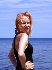 Portrait of a smiling blonde teenage girl in a black swimsuit against the backdrop of the sea horizon