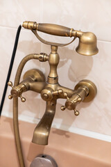 Close-up of elegant golden retro bathtub faucet with vintage style handles and shower head, shining metallic finish and classic bathroom design element