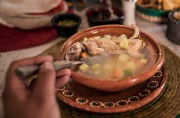 POV photo of Rat broth, a typical dish from the state of Zacatecas, Mexico, accompanied by chopped vegetables and a whole field rat, served in a clay dish.

