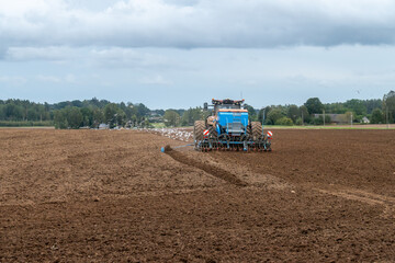 Obraz premium Tractor plowing and sowing farmland with seagulls flying around, rural countryside agriculture landscape with cultivated soil, forest and cloudy sky