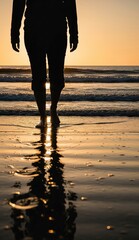 Silhouette of a person walking on a beach at sunset reflection visible