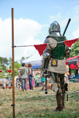 Medieval reenactor dressed in full suit of armor with sword and shield. Knight in protective gear participates in historical festival outdoors.