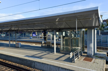 Modern train station platform with glass elevator and shelter roof.