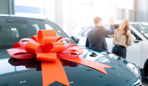 Celebratory car purchase at dealership, happy customers and new vehicle with red bow