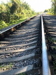 Railway tracks stretch into the distance surrounded by lush greenery under the bright sun