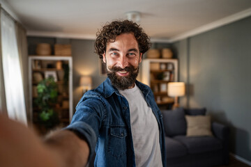 Obraz premium Cheerful bearded man taking selfie at home