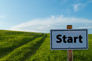 Schild Start vor grüner Wiese und blauem Himmel freier Horizont