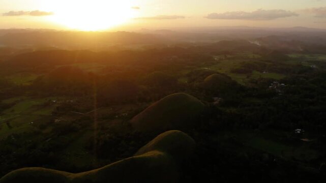 The sun sets over the chocolate hills in bohol, philippines, creating a golden glow