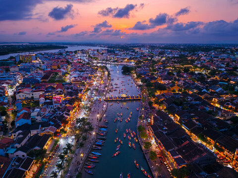 Aerial view of famous landmark bridge of ancient town Hoi An, Vietnam at sunset with lantern-lit boats on thu bon river