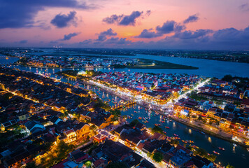 Fototapeta premium Aerial view of Hoi An at sunset with illuminated streets and tranquil river scene, famous ancient town of Vietnam