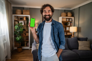 Smiling man presenting smartphone with green screen indoors