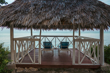 Private thatched roof cabana with ocean view and lounge chairs.