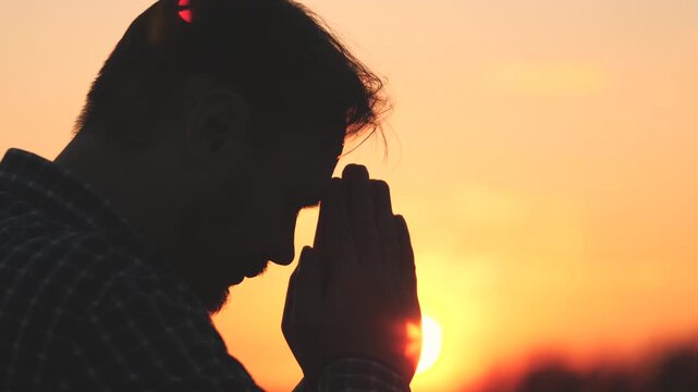 Man praying, man folded her hands in prayer silhouette at sunset. slow motion video lifestyle, man folded her hands in prayer pray to god, asks forgiveness for sins of repentance, believing man.