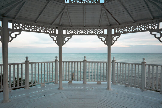 Wide shot of a gazebo by the sea surrounded by beautiful greenery.