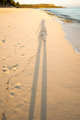 Long shadow cast on a serene beach at sunset, highlighting nature's beauty.