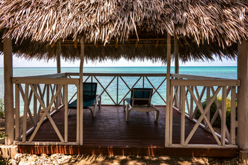Serene seaside gazebo with straw roof and lounge chairs by the tranquil sea.