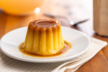 Vanilla pudding with caramel sauce on plate on wooden table.