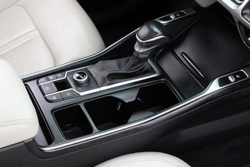 Car center console with black leather gear shifter, control buttons, rotary dial, dual cup holders, and light leather trim, designed for functionality and modern driving comfort.