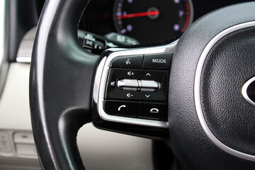 Close-up of a black leather steering wheel with integrated control buttons, including volume, mode...