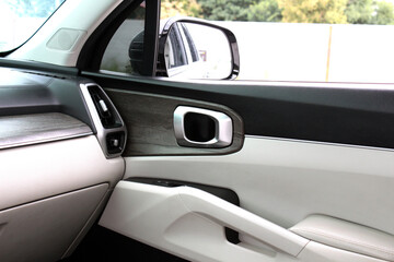 Car interior front passenger door with two-tone design. Soft beige leather armrest, matte metallic...