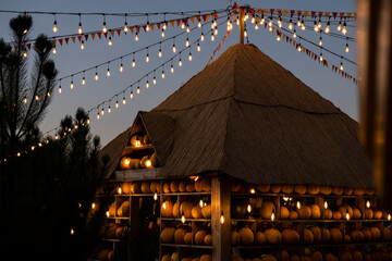 Rustic autumn evening with pumpkin house with warm glowing string lights and colorful flags. Cozy festive atmosphere perfect for fall, harvest festivals, Halloween and Thanksgiving celebrations.