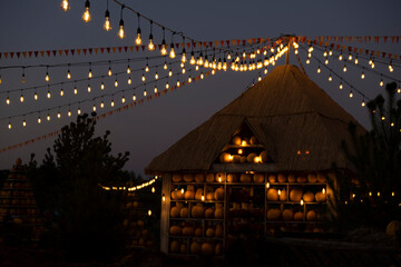 Rustic autumn evening with pumpkin house with warm glowing string lights and colorful flags. Cozy festive atmosphere perfect for fall, harvest festivals, Halloween and Thanksgiving celebrations.