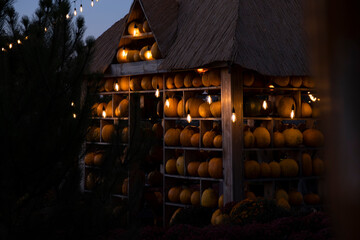 Atmospheric autumn evening with pumpkin house, illuminated by warm glowing string lights and vintage bulbs. Cozy seasonal mood for fall, harvest, farmers markets, Halloween Thanksgiving themes.