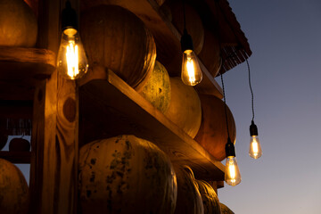 Pumpkins on wooden shelves illuminated by warm glowing vintage bulbs. Cozy rustic autumn atmosphere background for fall, harvest, farmers markets and Halloween themes. Happy Thanksgiving Day.