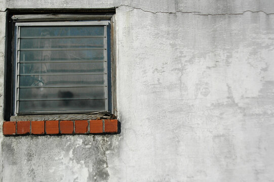 A single window with a red brick sill on a weathered white concrete wall, lots of space for adding your own text. Perfect for illustrating the effects of nature and weather on the built environment
