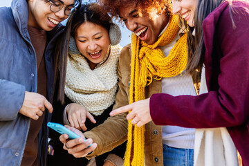 Multiracial friends laughing together watching social media content on phone. Technology and youth lifestyle concept