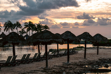 Beach loungers with thatched roofs at sunset by the peaceful coastline.