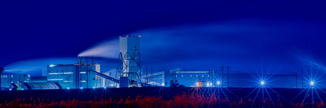 Potash mining and processing facility in Saskatchewan at night with illuminated structures and smoke under a dark sky.