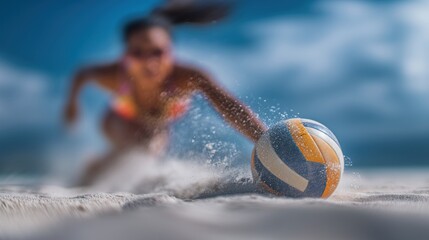 Close-up of a beach volleyball on the sand with a female player blurred in the background diving to hit it