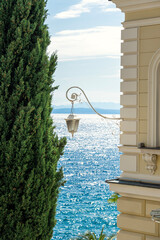 Elegant seaside view with a classic lamp, cypress tree, and shimmering blue sea in Opatija Croatia