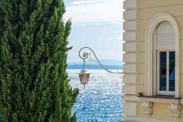 Elegant seaside view with a classic lamp, cypress tree, and shimmering blue sea in Opatija Croatia