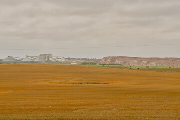 A potash plant with multiple dome-shaped storage buildings and conveyors viewed across farmland under cloudy skies in Saskatchewan, Canada.