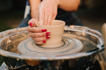Young woman smiling while working with clay on pottery wheel. Girl shapes clay on the pottery wheel with smile. Smiling artisan shapes clay on the spinning pottery wheel.