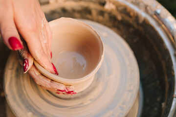 Smiling artisan shapes clay on the spinning pottery wheel. Young woman smiling while working with clay on pottery wheel. Girl shapes clay on the pottery wheel with smile.