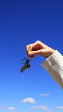 Womans hand holds silver apartment keys with a house-shaped keychain. Happy purchase of your own property or renting a house in a good area. Realtor, broker, real estate transaction.
