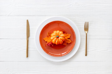 Top view of festive Thanksgiving table setting with pumpkin in plate and cutlery - autumn leaves...