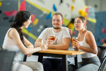 Young man and two young women chat at table on climbing wall after workout