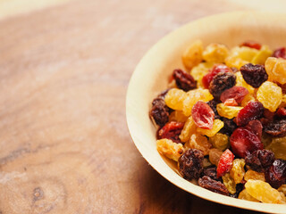 A bowl of dried fruit with yellow and red raisins, cranberries. The bowl is on a wooden table. Natural high sugar and glucose content. Popular snack.