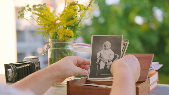 Hands holding vintage black and white photo baby family archive near wooden box and flowers, nostalgia ancestry genealogy memory history, Tracing family roots through images, journey into ancestry
