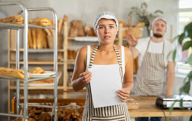 In bakery, frustrated female employee during quarrel with guy boss. Girl with documents in hands argues with entrepreneur, owner of bakery, listens to insults from manager